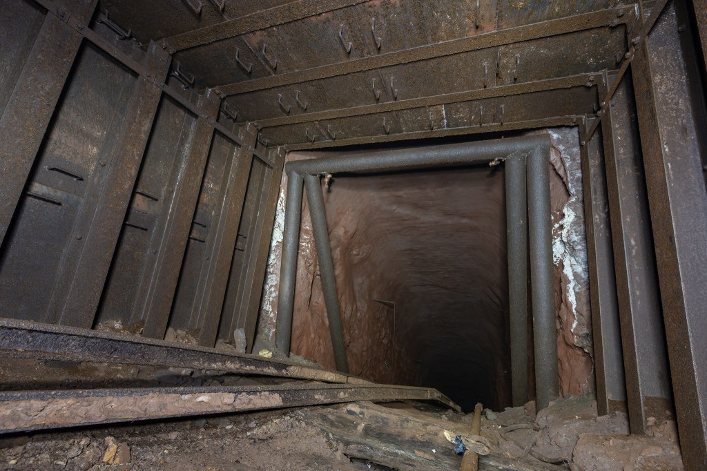 View looking down a deep mine shaft with metal supports and dirt walls.