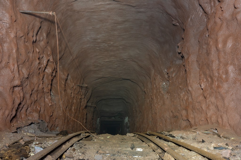 An underground tunnel with textured walls, showing railway tracks and debris on the ground
